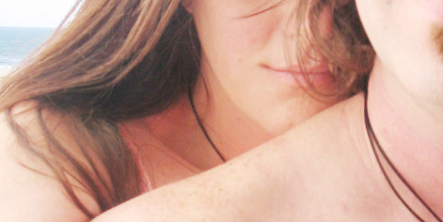 a closeup of a woman's face and arm reaching over a man's naked shoulder with the side of his face exposed