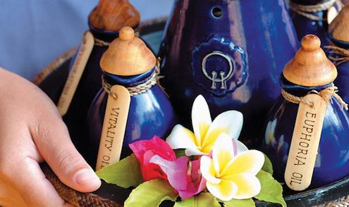 Two hands carrying a tray of blue clay bottles for an ayurvedic treatment