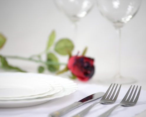 closeup of dinner table setting with a red rose to illustrate what we consider romantic