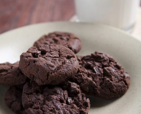 Cloesup of double chocolate almond cookies on a white plate with a tall glass of milk