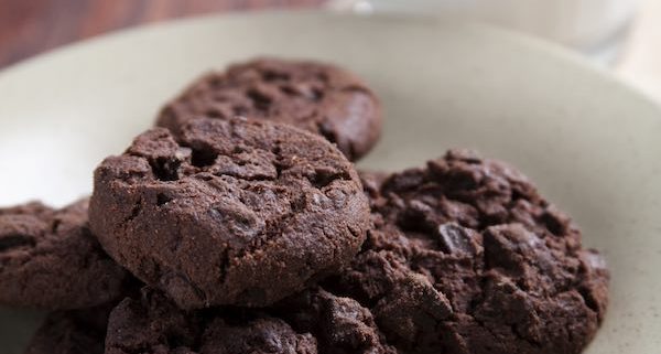 Cloesup of double chocolate almond cookies on a white plate with a tall glass of milk