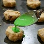 closeup of spoon putting green icing on icing cookies