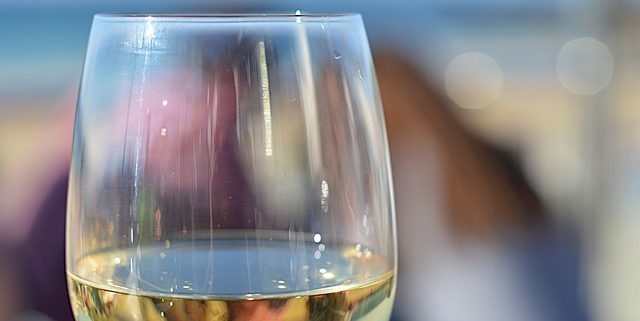 Glass of white wine outdoors with the blurry outline of a man and woman in the background