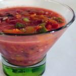 closeup of heirloom tomato gazpacho in a clear glass bowl with a green glass base
