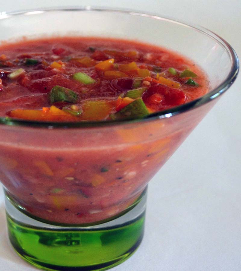 closeup of heirloom tomato gazpacho in a clear glass bowl with a green glass base