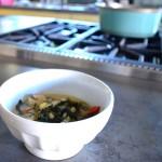 Coconut and Chicken Stew in a white bowl beside a stove with a blue stockpot