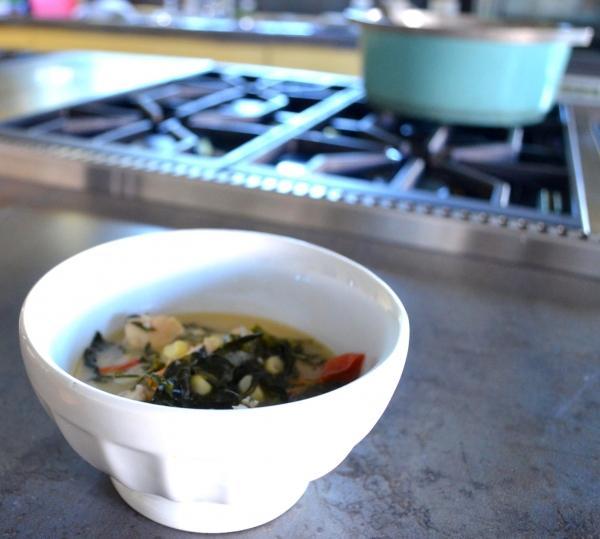 Coconut and Chicken Stew in a white bowl beside a stove with a blue stockpot