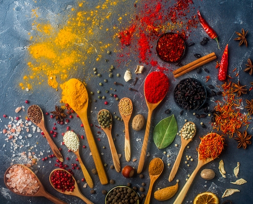 a rainbow of spices on cooking spoons to illustrate cook with spices