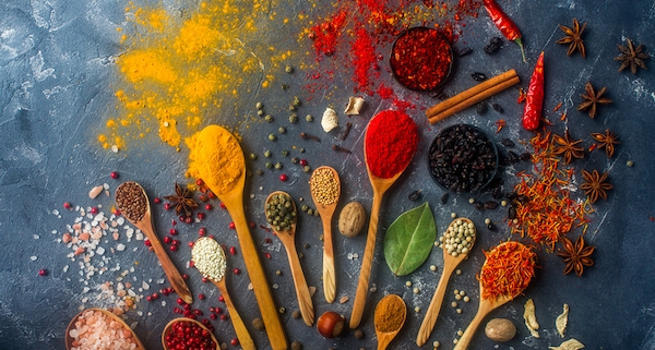 a rainbow of spices on cooking spoons to illustrate cook with spices