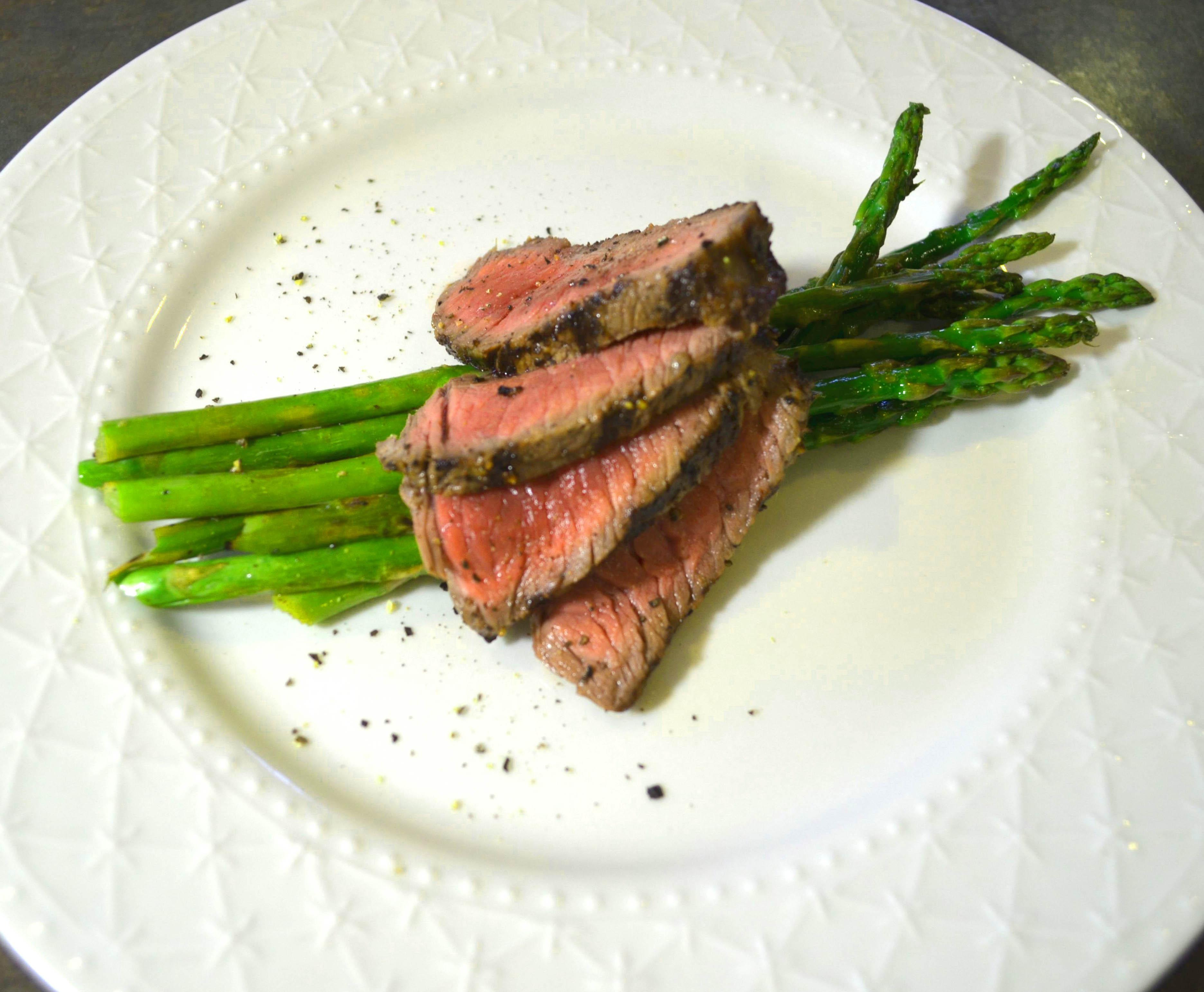 herb-marninated, grilled buffalo steak over asparagus on a white plate