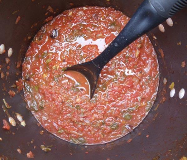 Puttanesca sauce in a pot with a black spoon