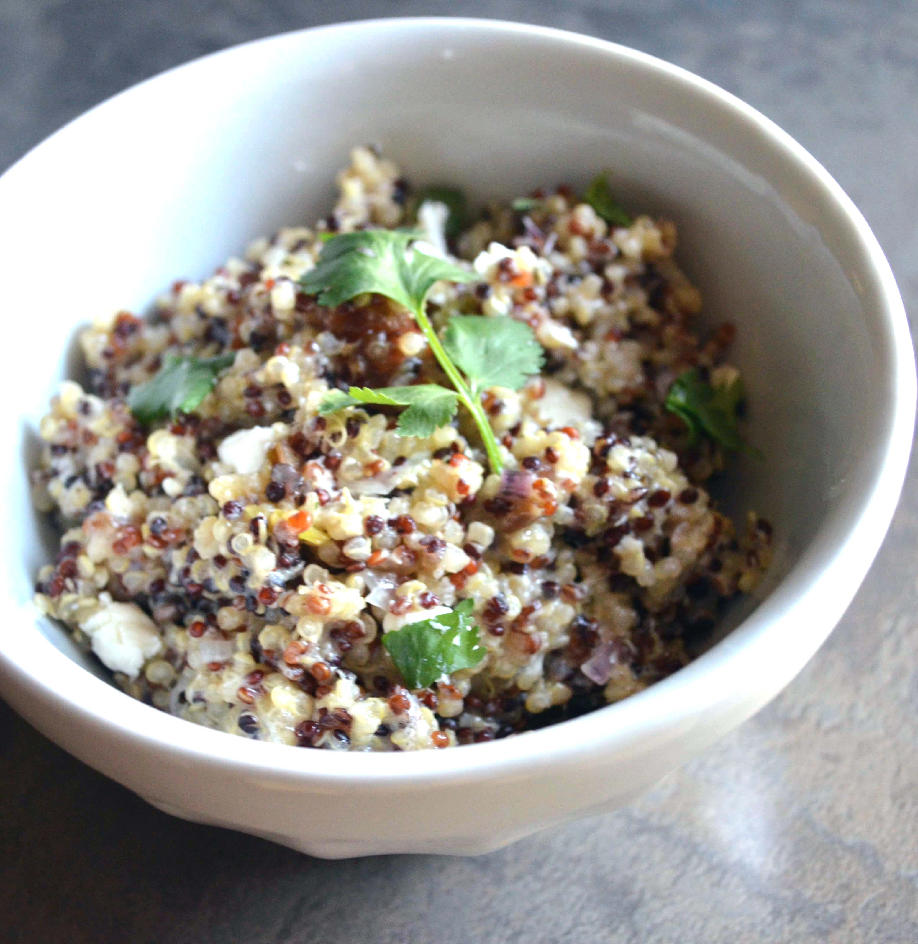 closeup of warm quinoa salad in a white bowl on a dark background