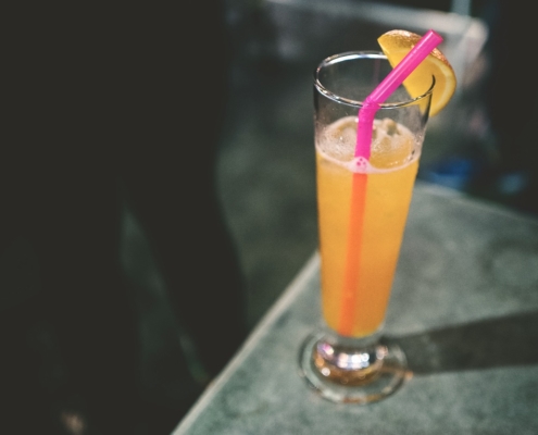 A thyme & honey gin fizz cocktail with a pink straw on a dark background