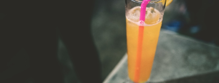 A thyme & honey gin fizz cocktail with a pink straw on a dark background