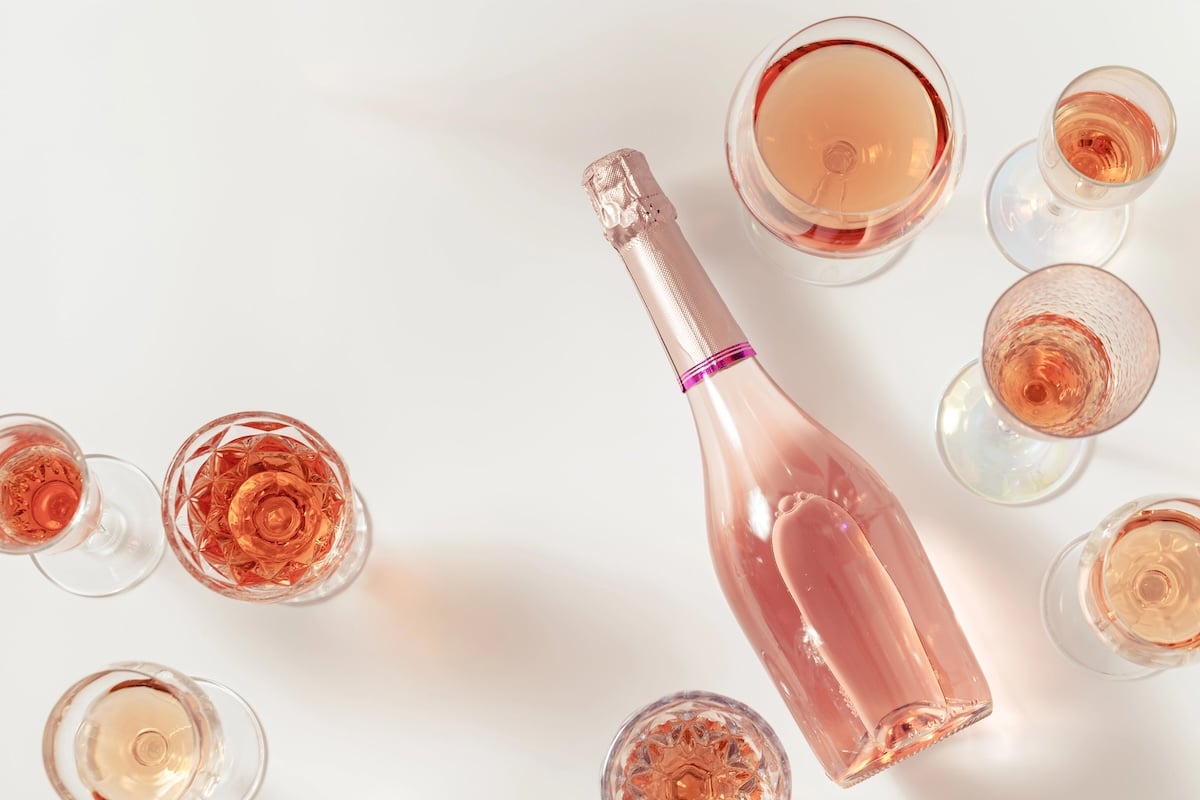 Champagne Might Get You Drunk Faster 3 bottle of rose champagne surrounded by glasses of various rose wines in different shades of pink on a white background
