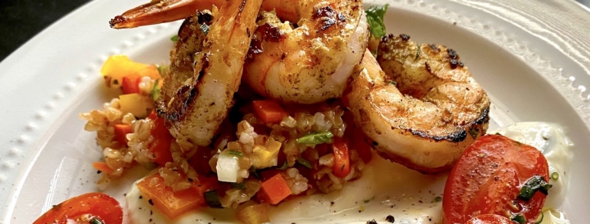 closeup of healthy shrimp recipe on top of bulgar salad and yogurt sauce on a white plate with picked grape tomatoes