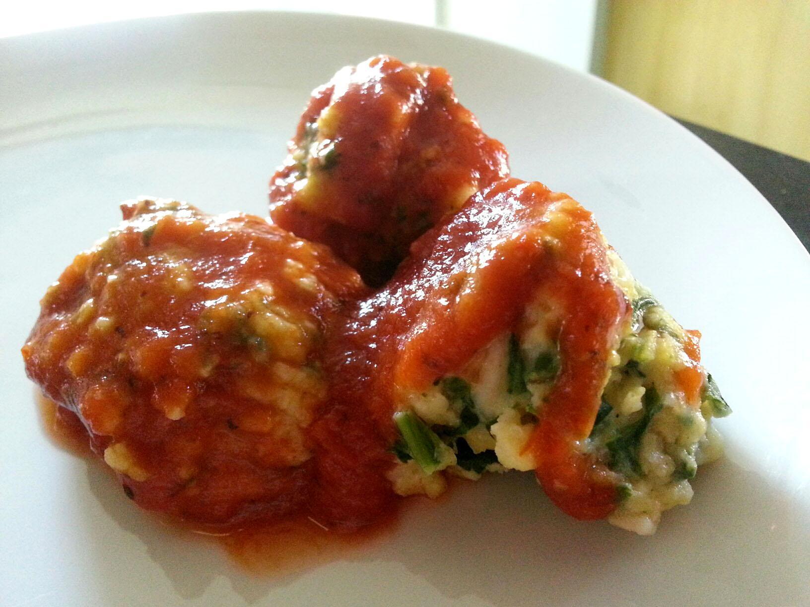 closeup of three ricotta gnudi with marinara on a white plate