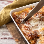 closeup of meatless lasagna in a baking dish with someone cutting it with a chef's knife