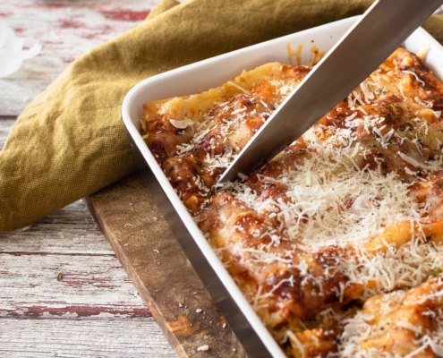 closeup of meatless lasagna in a baking dish with someone cutting it with a chef's knife