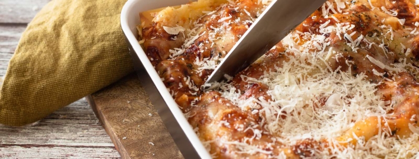 closeup of meatless lasagna in a baking dish with someone cutting it with a chef's knife