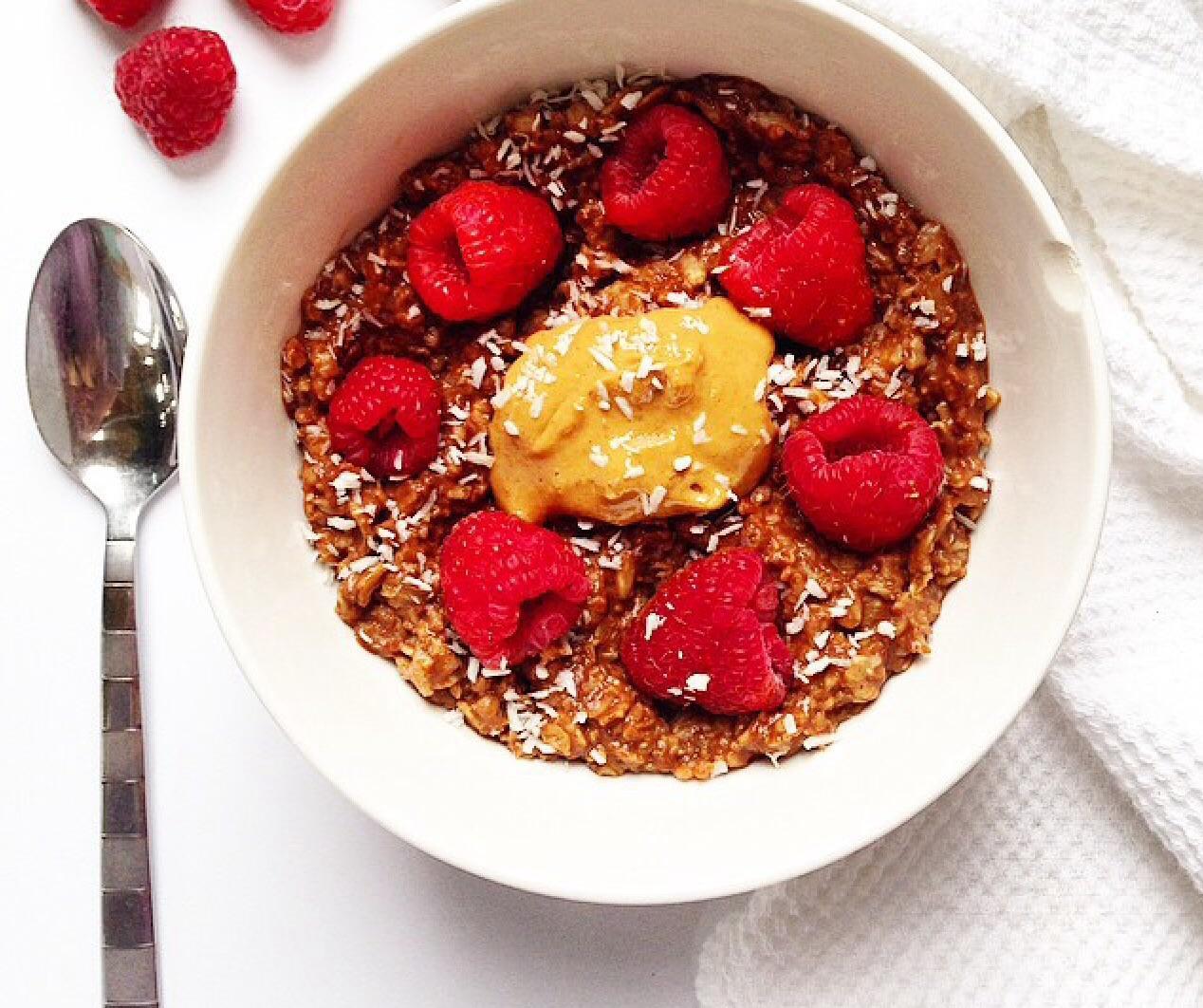 Cacao Raspberry Oats in a white bowl on a white background with a silver spoon to the left of the bowl