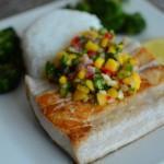 Closeup of seared mahi-mahi with fresh mango salsa and rice in the background on a white plate