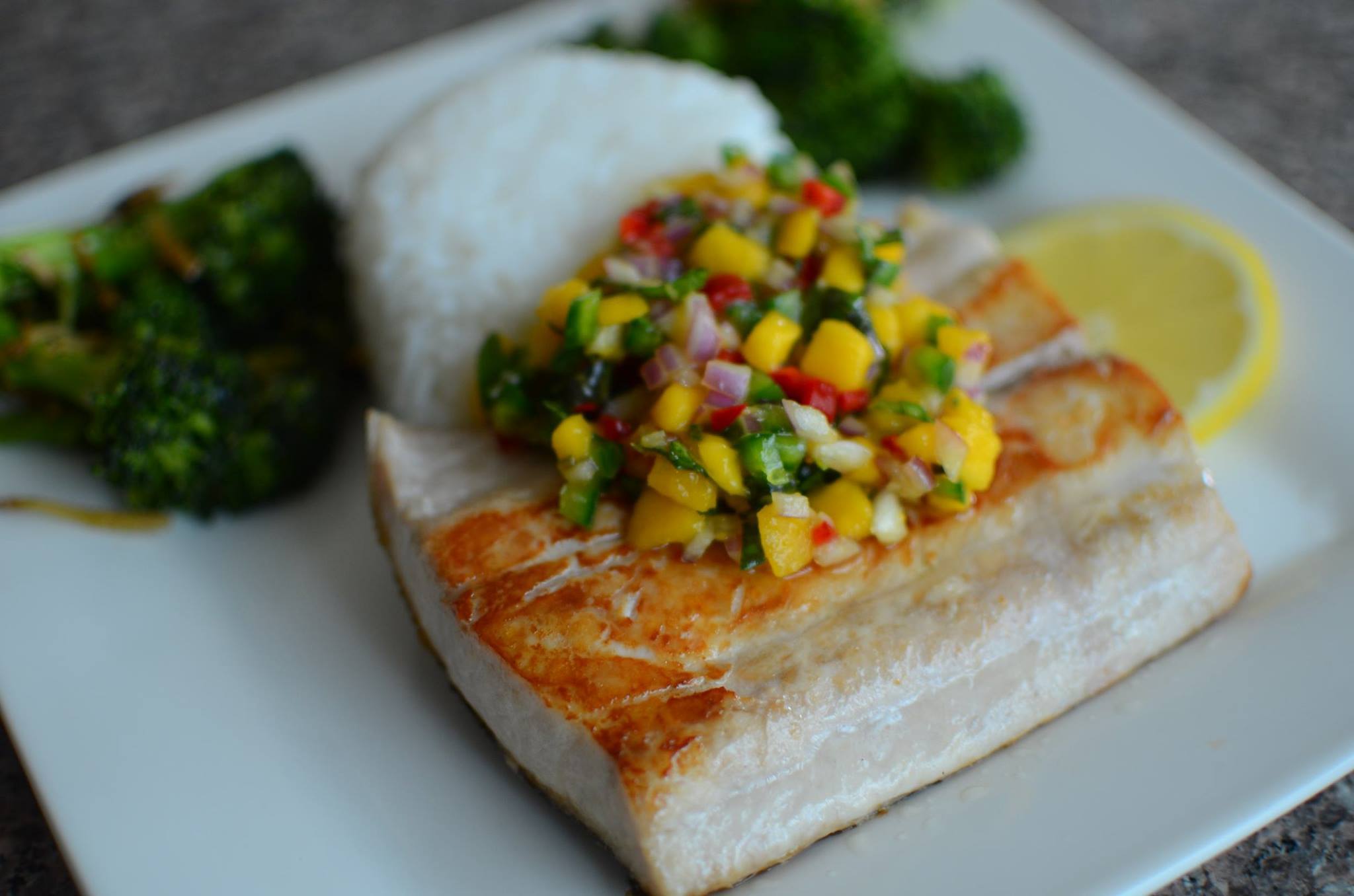 Closeup of seared mahi-mahi with fresh mango salsa and rice in the background on a white plate