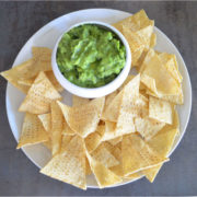 kale guacamole in a white ceramic bowl on a white plate with tortilla chips