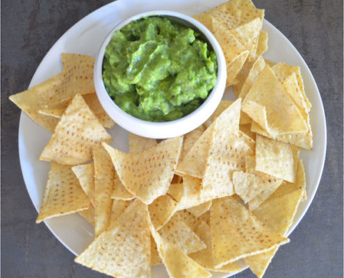 How to Make Kale Guacamole & Why You're Going to Love It! 9 kale guacamole in a white ceramic bowl on a white plate with tortilla chips