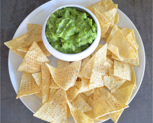 kale guacamole in a white ceramic bowl on a white plate with tortilla chips