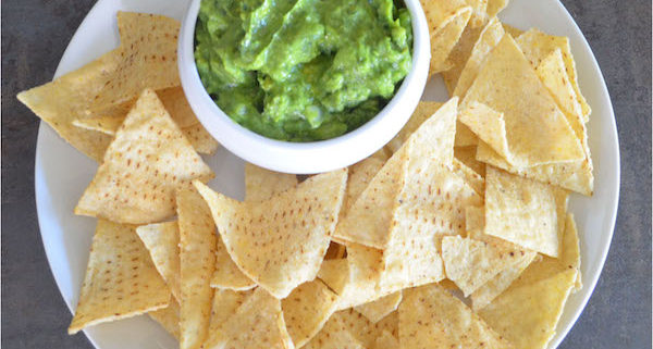 kale guacamole in a white ceramic bowl on a white plate with tortilla chips