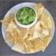 kale guacamole in a white ceramic bowl on a white plate with tortilla chips