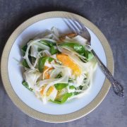 shaved fennel salad with citrus and arugula on a white plate with gold trim and a fork angled on the righthand side