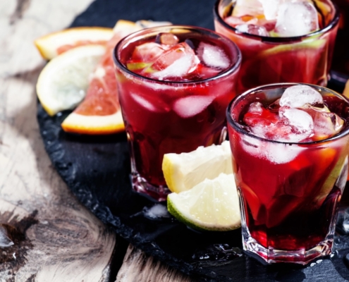 three glasses of red wine citrus sangria on a black tray with wedges of citrus for accents
