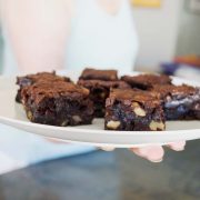 gluten-free chocolate chunk brownies on a white plate being held by a woman's hand