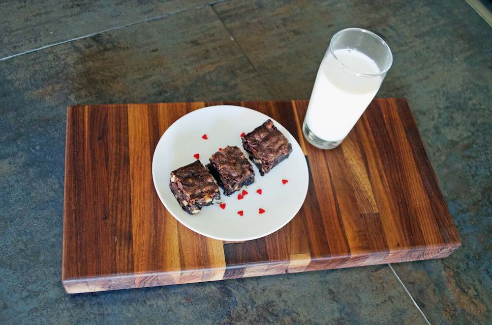 Gluten Free Chocolate Chunk Brownies with Balsamic Cherries and Walnuts on a wooden board with a glass of milk