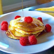 Coconut Pancakes Recipe with Chia Seeds 2 Maple Syrup Poured Over Chia Seed and Coconut Pancakes On White Plate with Raspberries