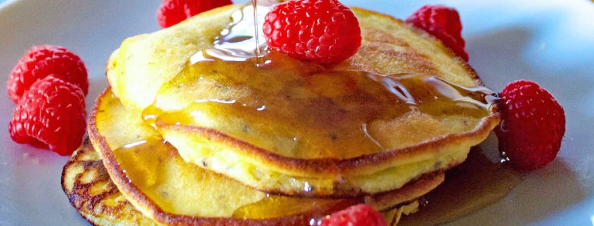 Maple Syrup Poured Over Chia Seed and Coconut Pancakes On White Plate with Raspberries