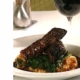 Closeup of red wine short ribs with figs in a white dish with a glass of wine and a silver fig in the backgorund