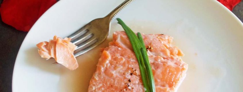 closeup of sexy salmon poached in rosé wine sauce on a white plate with a red napkin