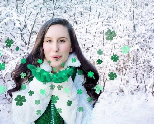 Dark haired woman in white standing in snow blowing green metallic shamrock kisses