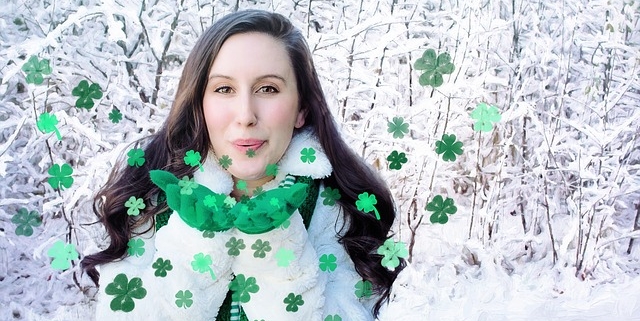 Dark haired woman in white standing in snow blowing green metallic shamrock kisses