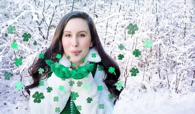 Dark haired woman in white standing in snow blowing green metallic shamrock kisses