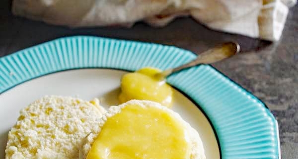 passion fruit curd on a scone sitting on a white plate with turquoise trim