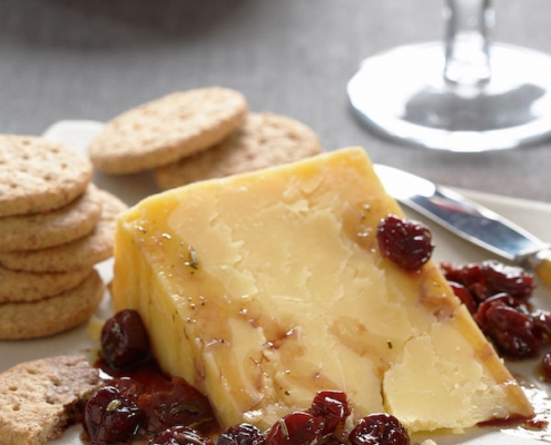 closeup of wine marinated cherries with white cheddar with a glass of red wine and a stack of white plates in the background