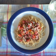 whole wheat spaghetti with raw tomato sauce on a plaid placemat with a glass of white wine