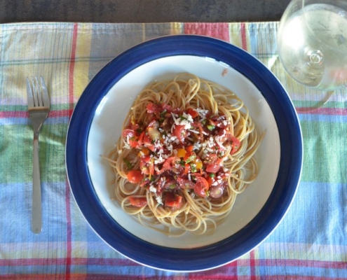 whole wheat spaghetti with raw tomato sauce on a plaid placemat with a glass of white wine