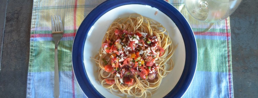 whole wheat spaghetti with raw tomato sauce on a plaid placemat with a glass of white wine