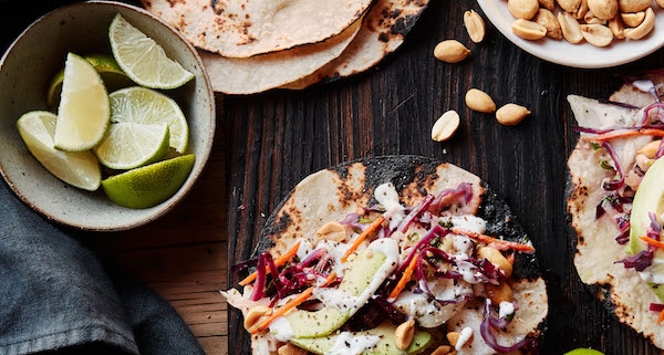 closeup of Asian fish tacos with a bowl of tortillas and a second bowl of cut limes on the left side