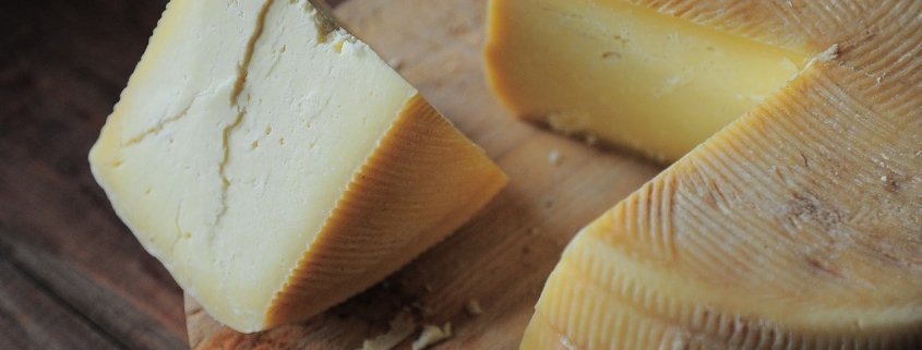 closeup of wheel of cheese with slice taken out and sitting beside it on a cutting board